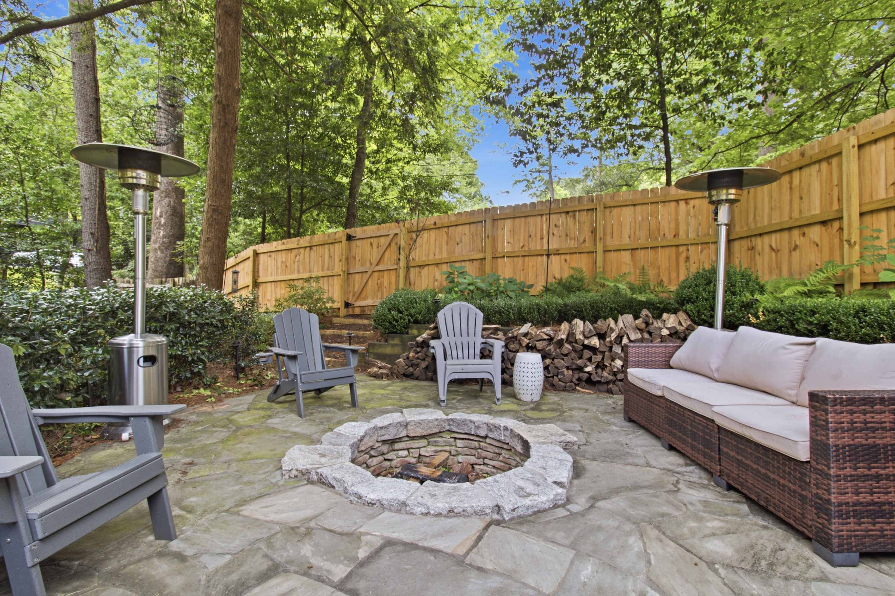Un patio exterior con un brasero, dos sillas Adirondack, un sofá de mimbre y una valla de madera.
