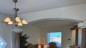 Un salon avec une table basse ronde, deux fauteuils, un lustre et une grande fenêtre.