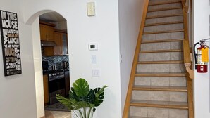 Un escalier menant à un deuxième étage, un coin cuisine avec des placards, une plante en pot et un panneau décoratif mural.