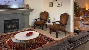 Un salon avec une cheminée, deux fauteuils, un canapé, un téléviseur et un tapis.