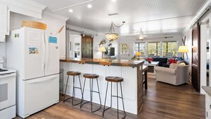 Une cuisine avec un îlot central en bois, des tabourets de bar, un réfrigérateur et un coin repas comprenant un canapé et une table.