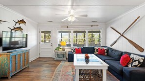 Un salon avec un téléviseur, un ventilateur de plafond, un canapé bleu et une table basse.