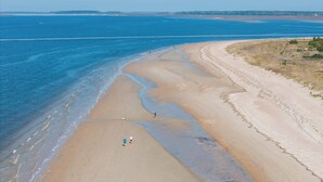 Une plage avec une longue étendue de sable, quelques personnes qui se promènent et une côte visible au loin.