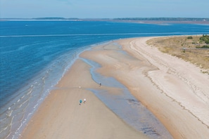 Ein Strand mit weitem Sandstreifen, ein paar Spaziergängern und einer entfernten Küstenlinie.