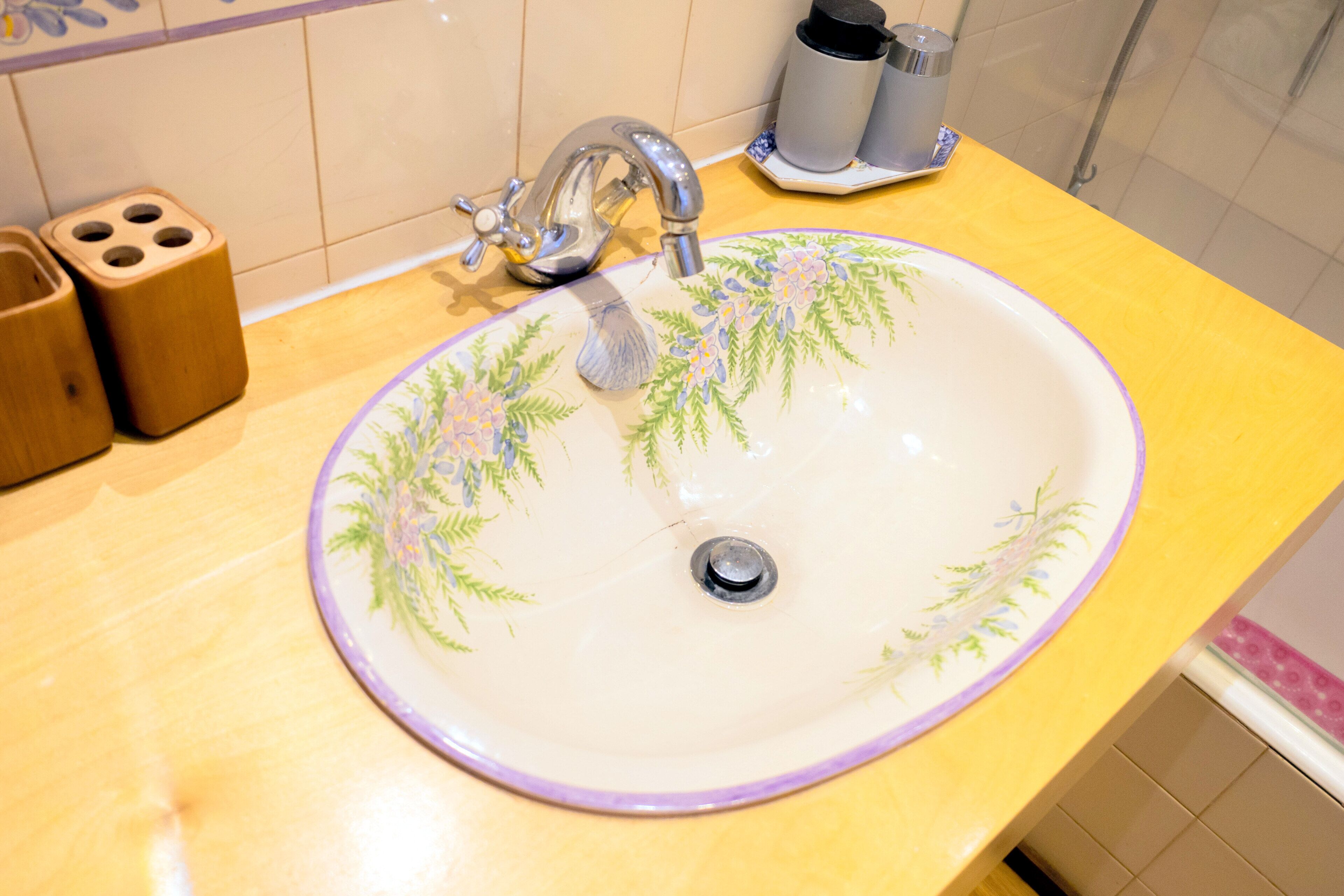 A bathroom sink with a floral design, a faucet, and a cup holder.