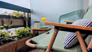 A green lounge chair with a striped pillow, a wicker basket, and a glass of orange juice on a balcony with potted plants. - ihTop | 4 Bedrooms | 3 Bathrooms | 3 Balconies (Espinho)