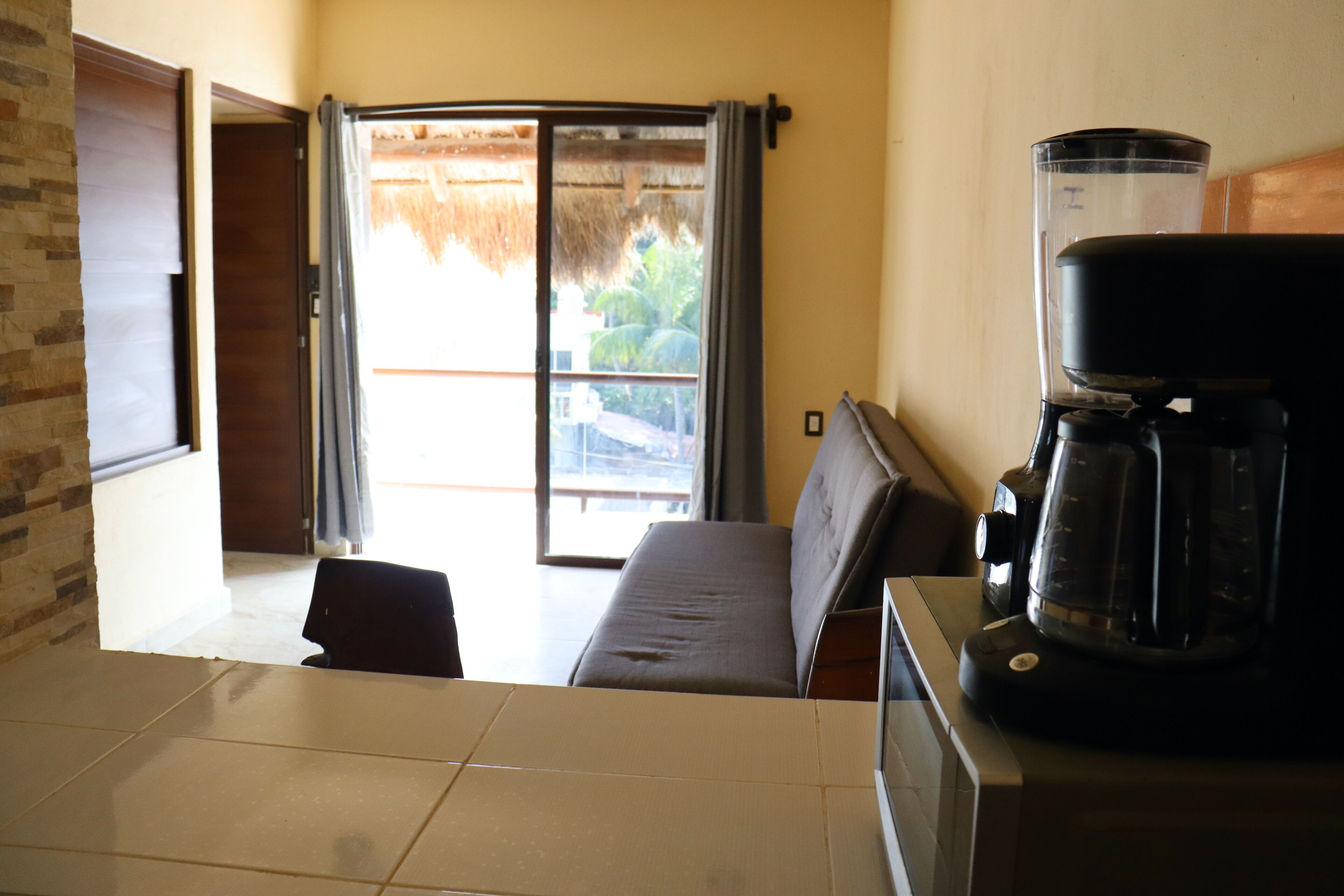 Una habitación con sofá, cafetera y puerta corrediza de vidrio que da a un balcón.
