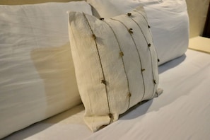 A bed with white bedding and a single decorative pillow with a textured pattern. - Jardin del Mar by ÓOL Hotels (Isla Holbox)