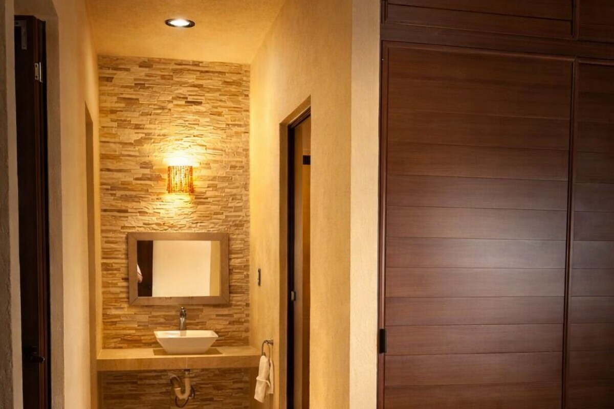 Quarto de hotel com guarda-roupa de madeira, banheiro com parede de pedra, pia e espelho.