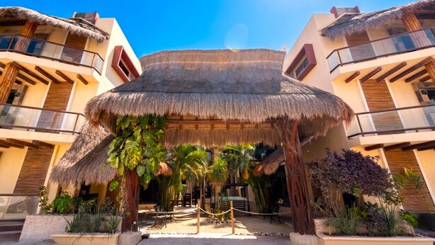 Un resort con una estructura central de techo de paja, varios balcones y plantas tropicales.