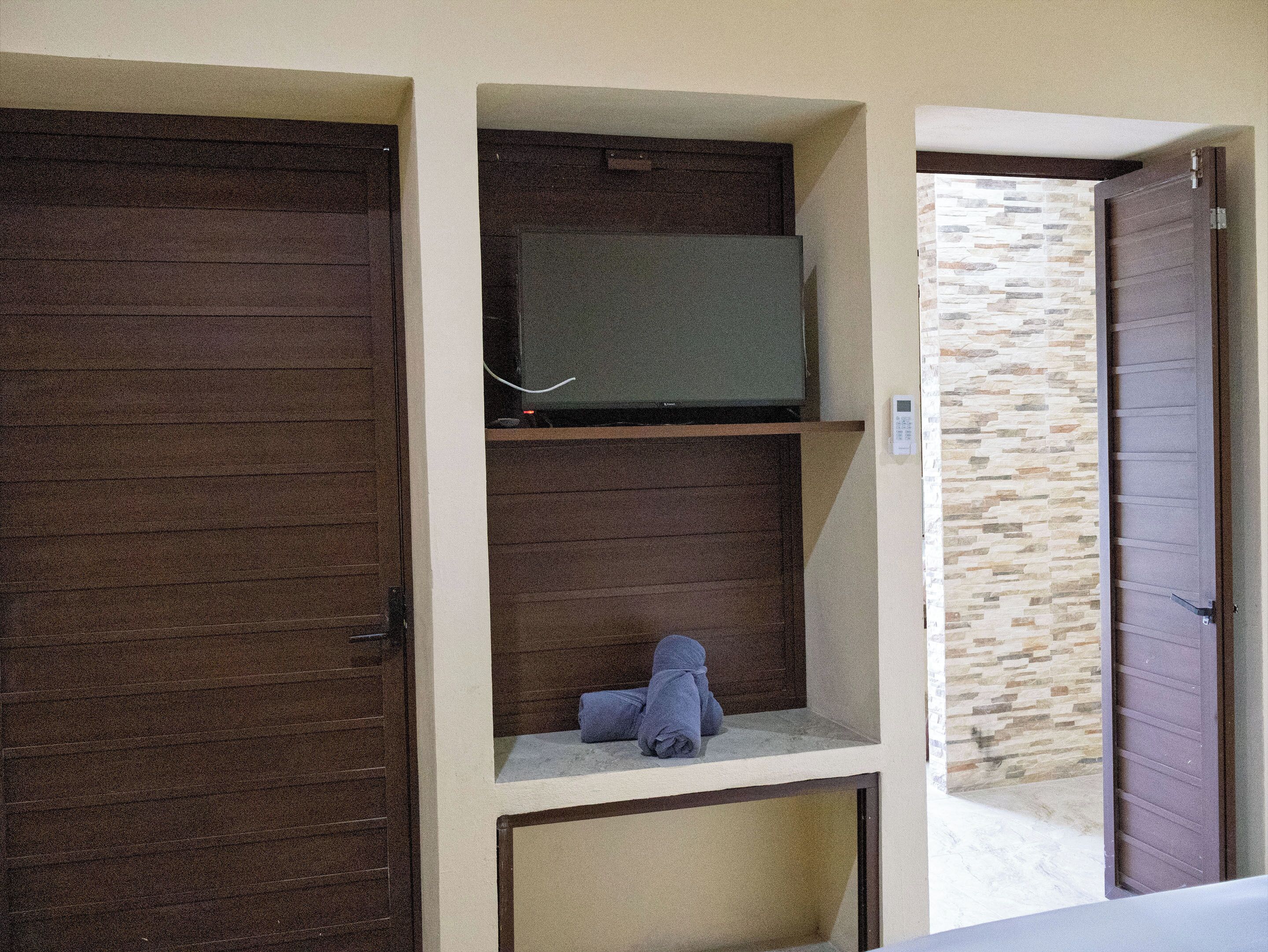 Um quarto com porta fechada, uma televisão em uma estante, uma toalha no chão e uma parede com padrão de pedra.