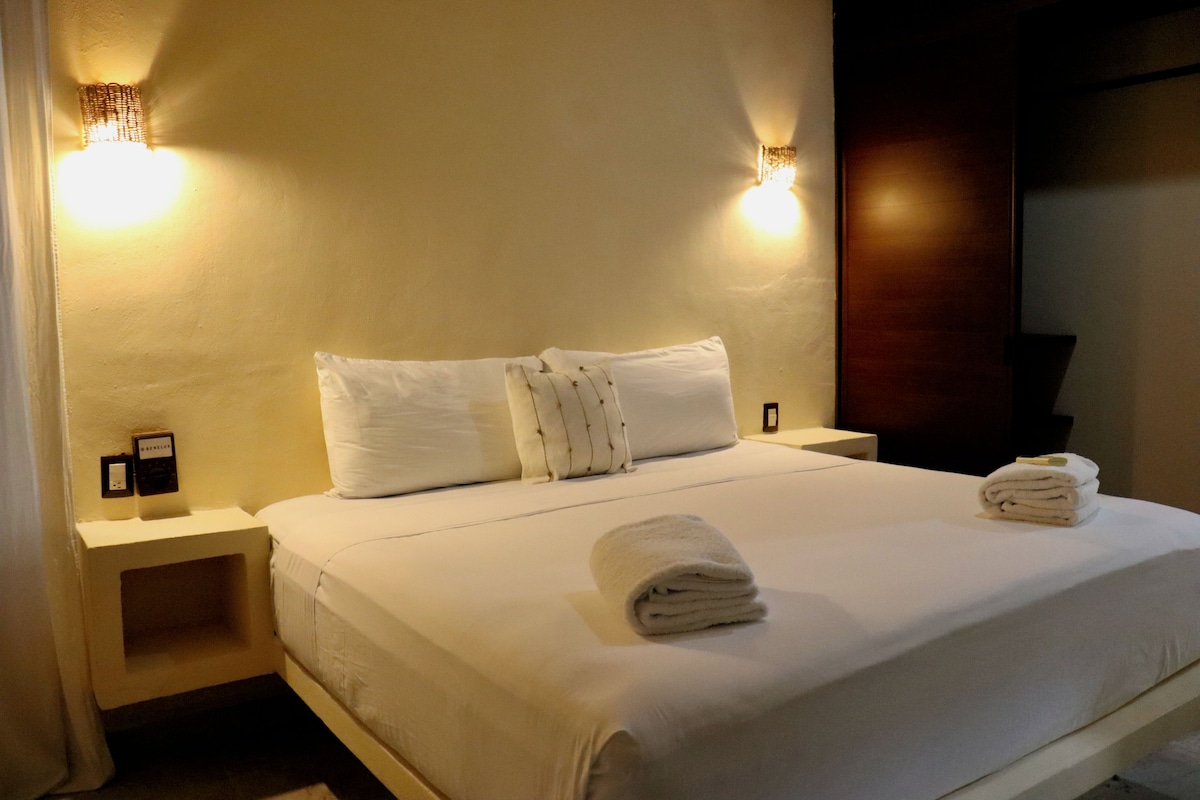 A hotel room with a large bed, two bedside tables, and wall-mounted lights.