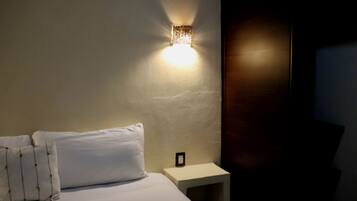Een hotelkamer met een bed, kussens, een nachtkastje en een wandlamp.