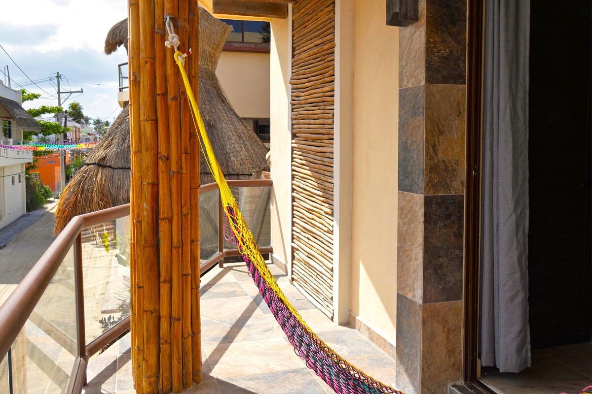 A balcony with a hammock, a thatched roof, and a stone wall.
