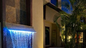 Una piscina con cascada, rodeada por un edificio de fachada de piedra y palmeras.