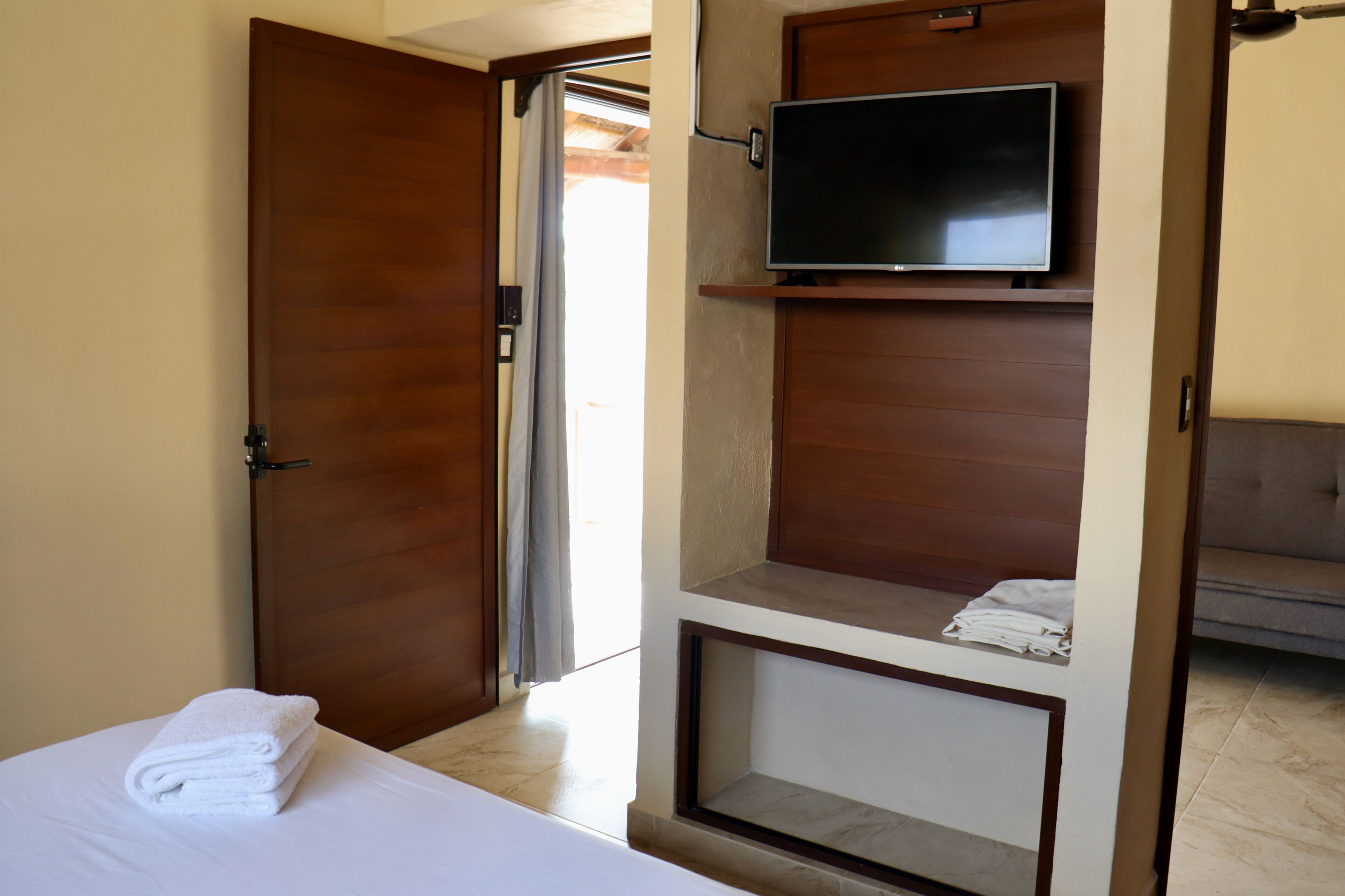 Habitació d'hotel amb un llit, un televisor fixat a un panell de fusta i una porta que condueix a una altra habitació.