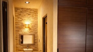Habitación de hotel con armario de madera, baño con pared de piedra, lavabo y espejo.