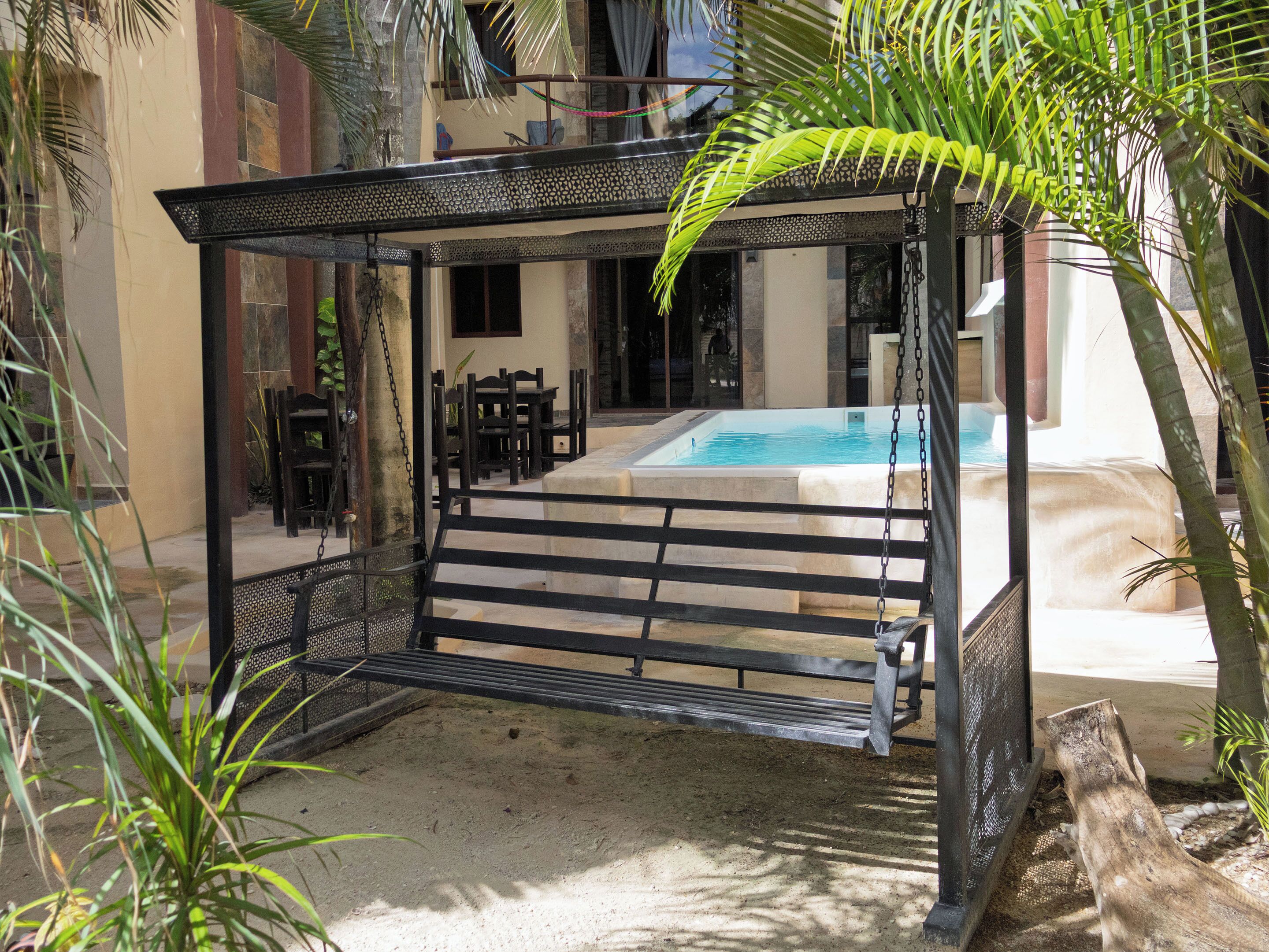 Un espace extérieur aménagé, abrité, avec une piscine en arrière-plan.