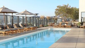 Ein Dachpool mit Liegestühlen und Sonnenschirmen, umgeben von einem hohen Zaun und Bäumen.