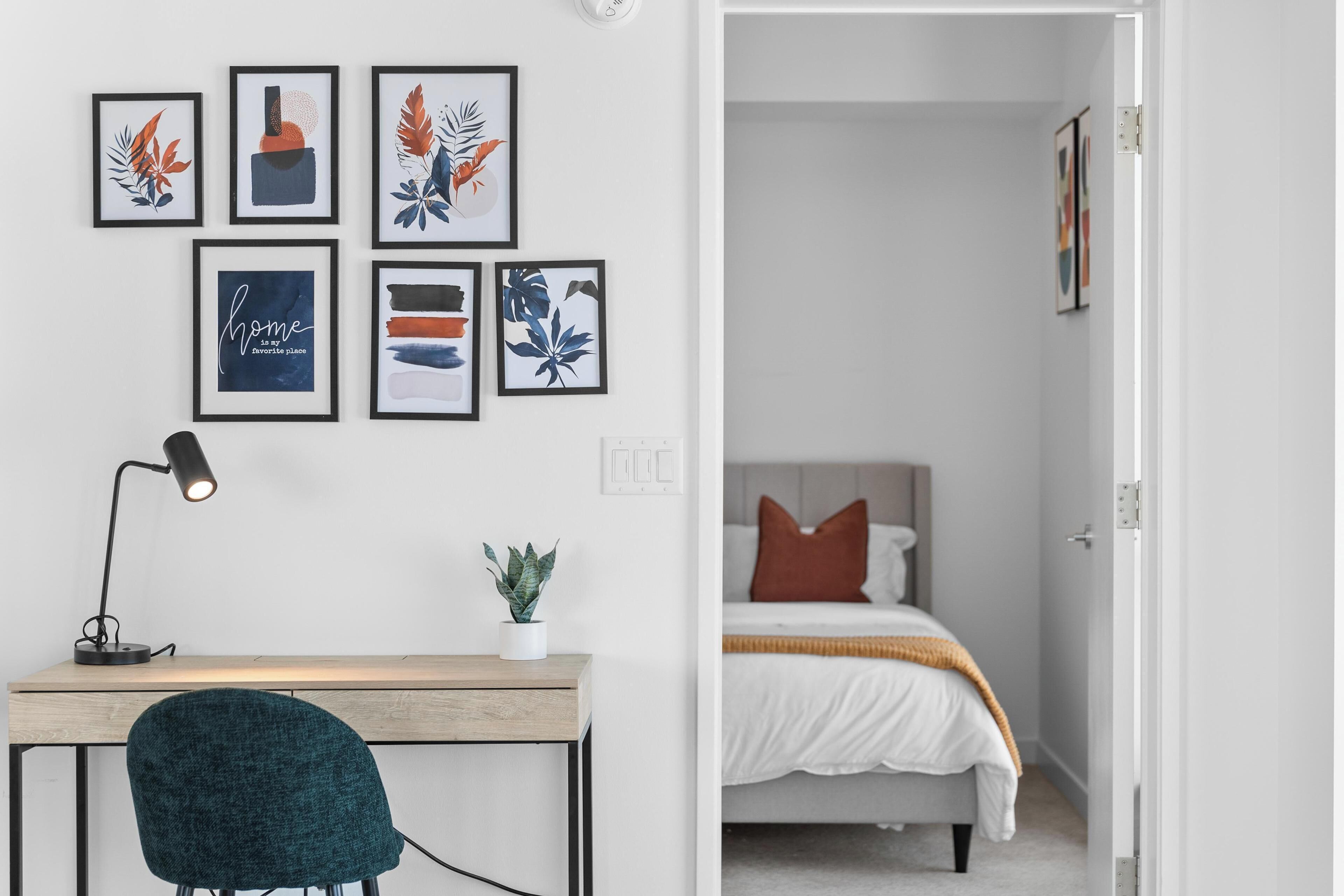Ein Zimmer mit Schreibtisch, Stuhl und einem Bett mit weißer und orangefarbener Decke.