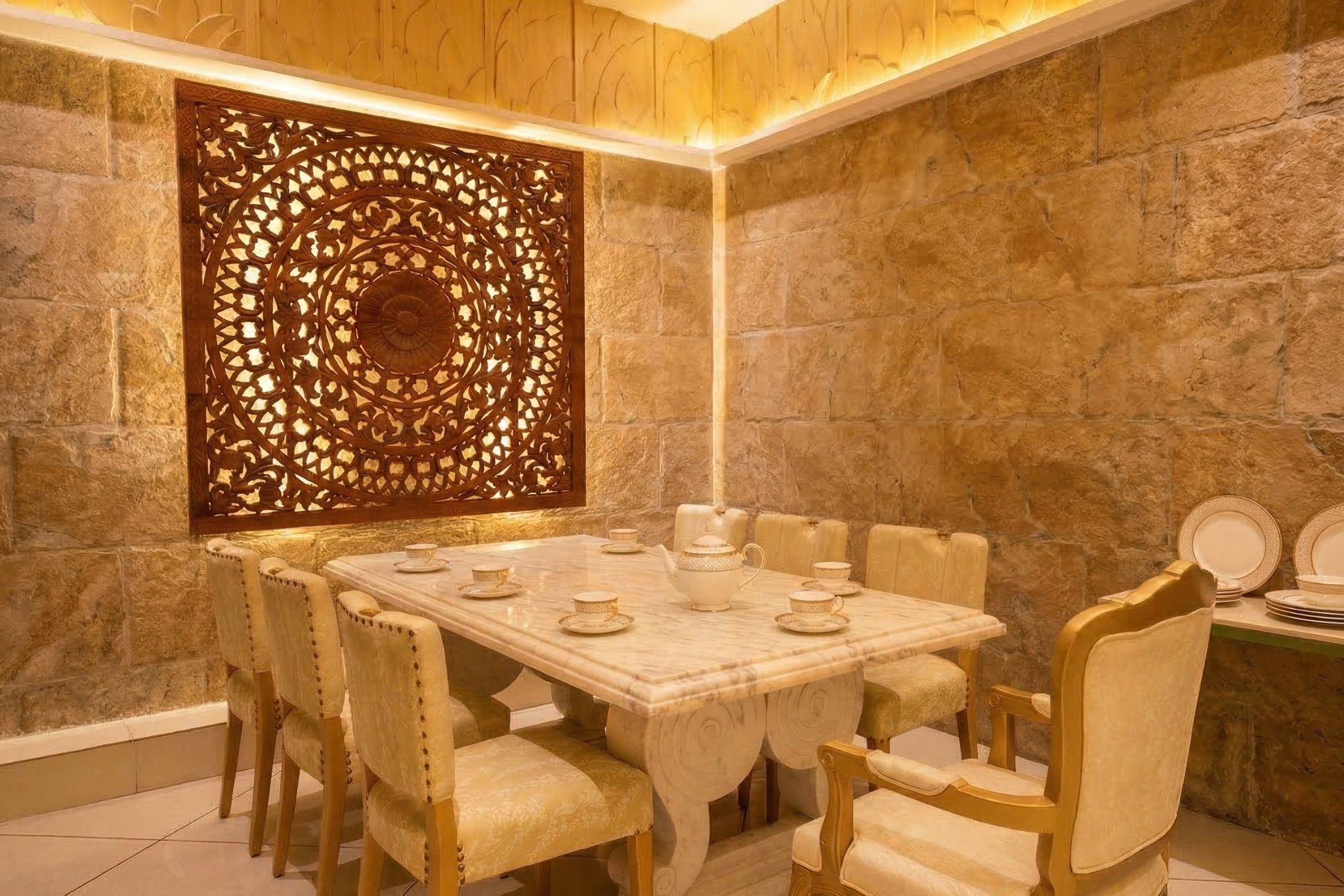 Uma área de refeições com mesa de mármore, cadeiras de madeira, painel decorativo e paredes de pedra.