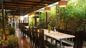 Un'area pranzo all'aperto con tavoli e sedie, circondata da piante e vegetazione.