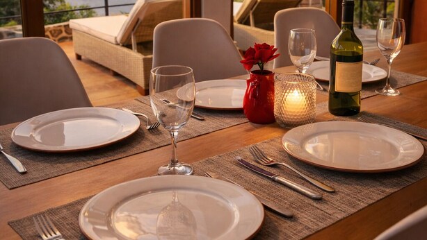 A dining table set for two with plates, cutlery, and wine glasses, overlooking a scenic mountain view.