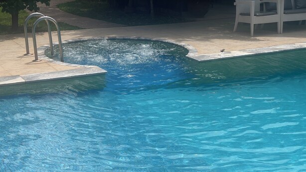 Una piscina con agua cristalina, un trampolín y una tumbona.
