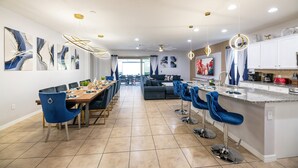 A modern kitchen with a central island, bar stools, and a dining area with a long table and chairs. - NEW!Racing Simulator|Game Room|Movie Room|Sleep 21 (Kissimmee)