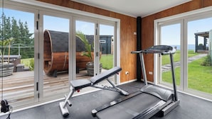 Un gimnasio en casa con cinta de correr, prensa y pesas, amplias puertas correderas de vidrio que dan a una terraza y zona exterior.