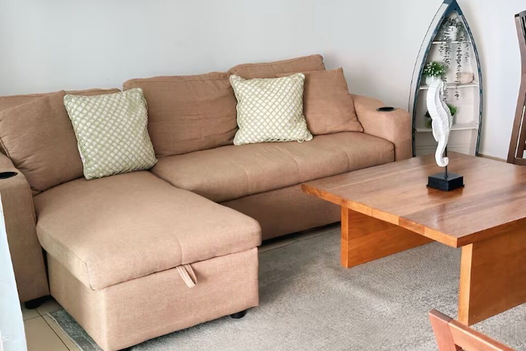 Un canapé d’angle beige avec des coussins assortis, une table basse en bois et un objet décoratif blanc posé sur la table.