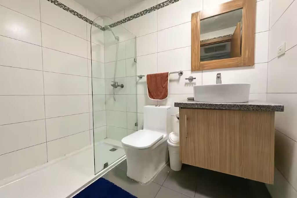 Une salle de bain avec une douche à parois de verre, des toilettes blanches, un meuble-lavabo en bois avec un évier et un miroir au-dessus du meuble-lavabo.