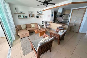 A living room with a sofa, chairs, a coffee table, and a dining table. There is a kitchen area with a refrigerator and cabinets. - Oceanfront 2-BR in Marbella  Private Beach + View (Playa Juan Dolio)