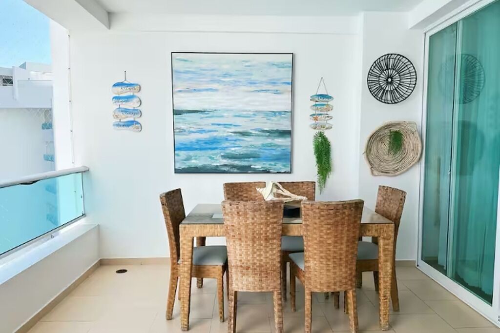 Un coin repas avec des chaises en osier et une table, une grande peinture abstraite et des éléments décoratifs suspendus au mur.