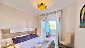 Een hotelkamer met een bed, een stoel, een nachtkastje en een balkon met een tafel en stoelen.