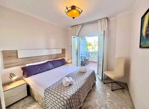 A hotel room with a bed, a chair, a nightstand, and a balcony with a table and chairs. - Sea front apartment in Playa Rocio, Puerto Banus with swimming pool and parking (Marbella)