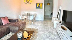 Een moderne woonkamer met een bank, een salontafel, een eettafel met stoelen, een kroonluchter en een televisie.