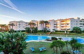 A hotel with multiple floors, outdoor swimming pools, and palm trees. - Sea front apartment in Playa Rocio, Puerto Banus with swimming pool and parking (Marbella)