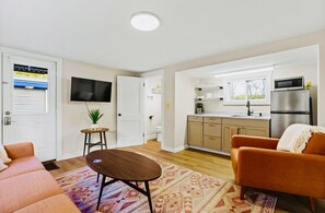 A compact living space with a kitchenette, a sofa, a small table, and a TV mounted on the wall.