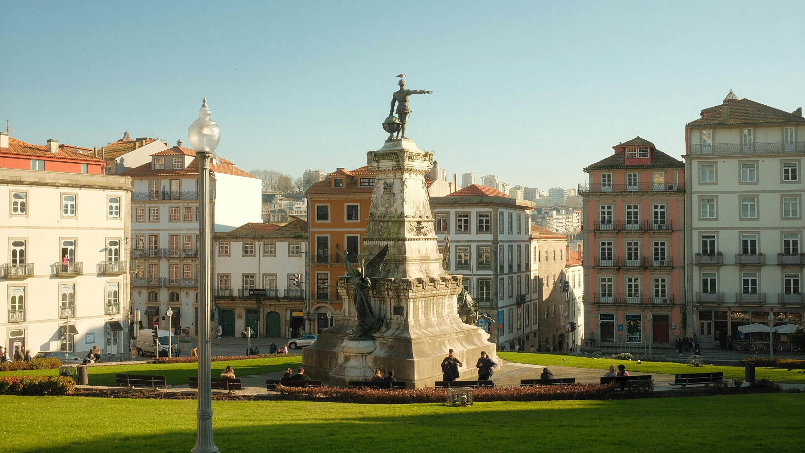 A city square with a central monument, surrounded by historic buildings with balconies.