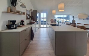 Una cocina moderna con una isla grande, luces colgantes y vistas a través de la puerta de cristal.