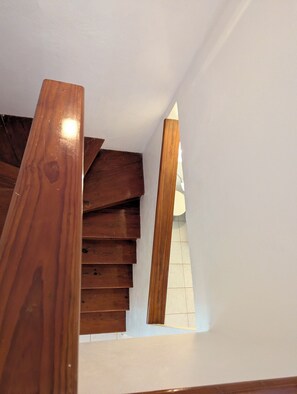 Eine Holztreppe mit weißer Wand und einem kleinen Fenster oben.