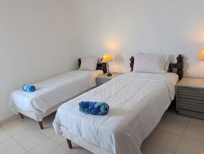 Ein Hotelzimmer mit zwei Einzelbetten, jeweils mit Holz Kopfteil, weißer Bettwäsche und einer Lampe auf den Nachttischen.