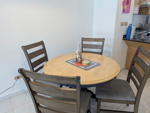 Ein runder Holztisch mit vier Stühlen, einer Glasvase mit Muscheln und einer farbenfrohen Tischmatte.