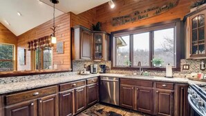 Una cucina con mobili in legno, piani di lavoro in granito, elettrodomestici in acciaio inossidabile e un'ampia finestra con vista sull'esterno.