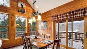 Una baita in legno con zona pranzo, ampie finestre e una terrazza.