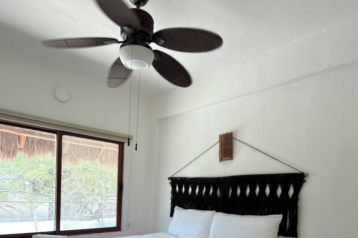 Un dormitorio con cama, ventilador de techo, mesita de noche y ventana con vistas.