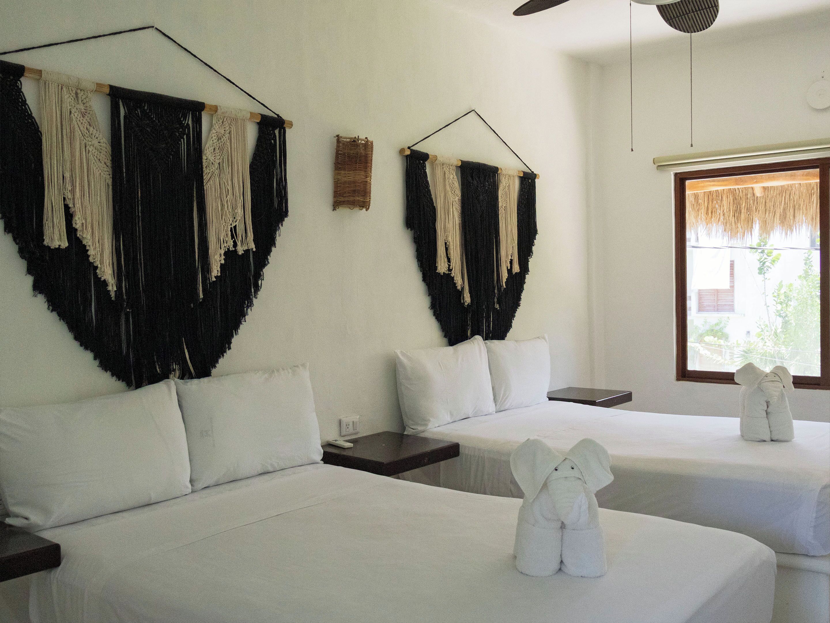 A hotel room with two beds, a small table, a nightstand, and a window with a view.