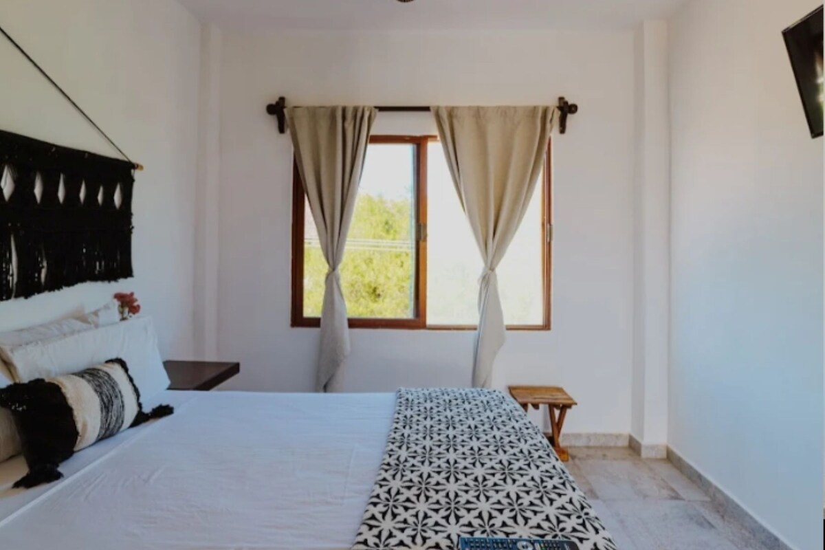 A bedroom with a bed, curtains, a small table, and a window.