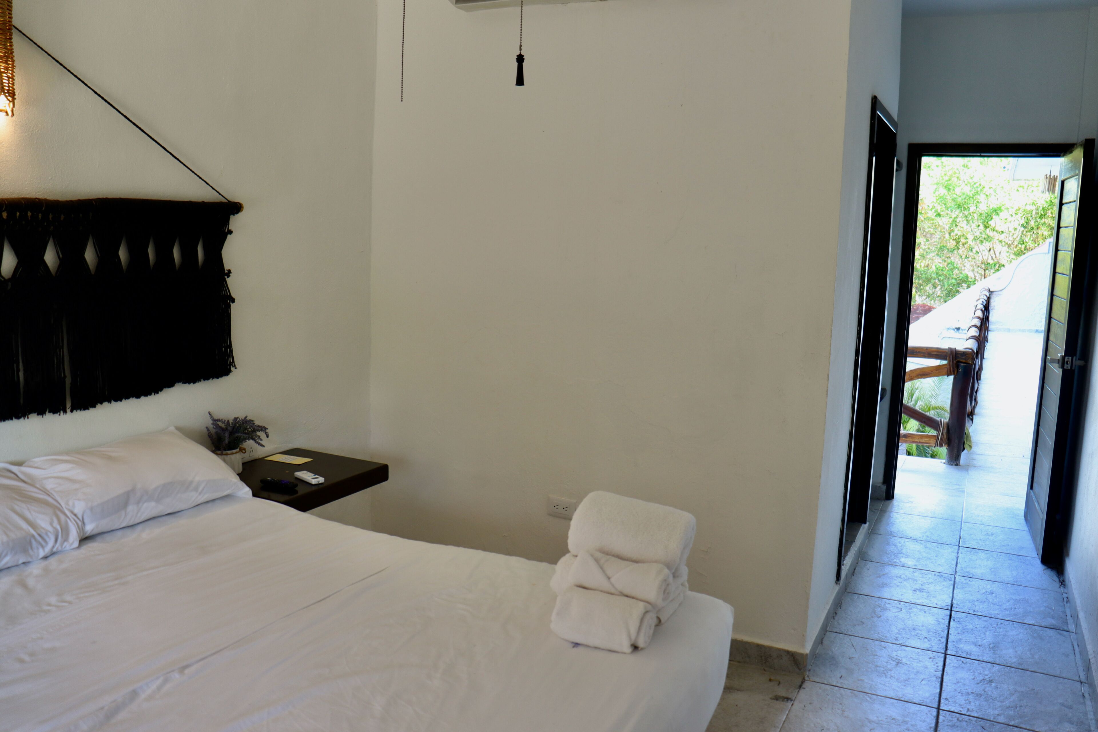 A bedroom with a bed, a nightstand, a wall-mounted light, and a view of an outdoor area through an open door.